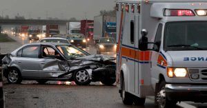 Damaged car on a busy highway beside an ambulance responding to a crash, representing the car accident work of Welcome Law Firm in Bridgeport