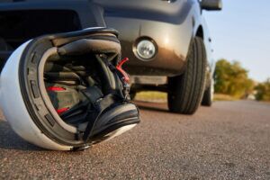 Damaged helmet resting on pavement near a vehicle after a motorcycle accident, illustrating the motorcycle accident practice of Welcome Law Firm in Bridgeport